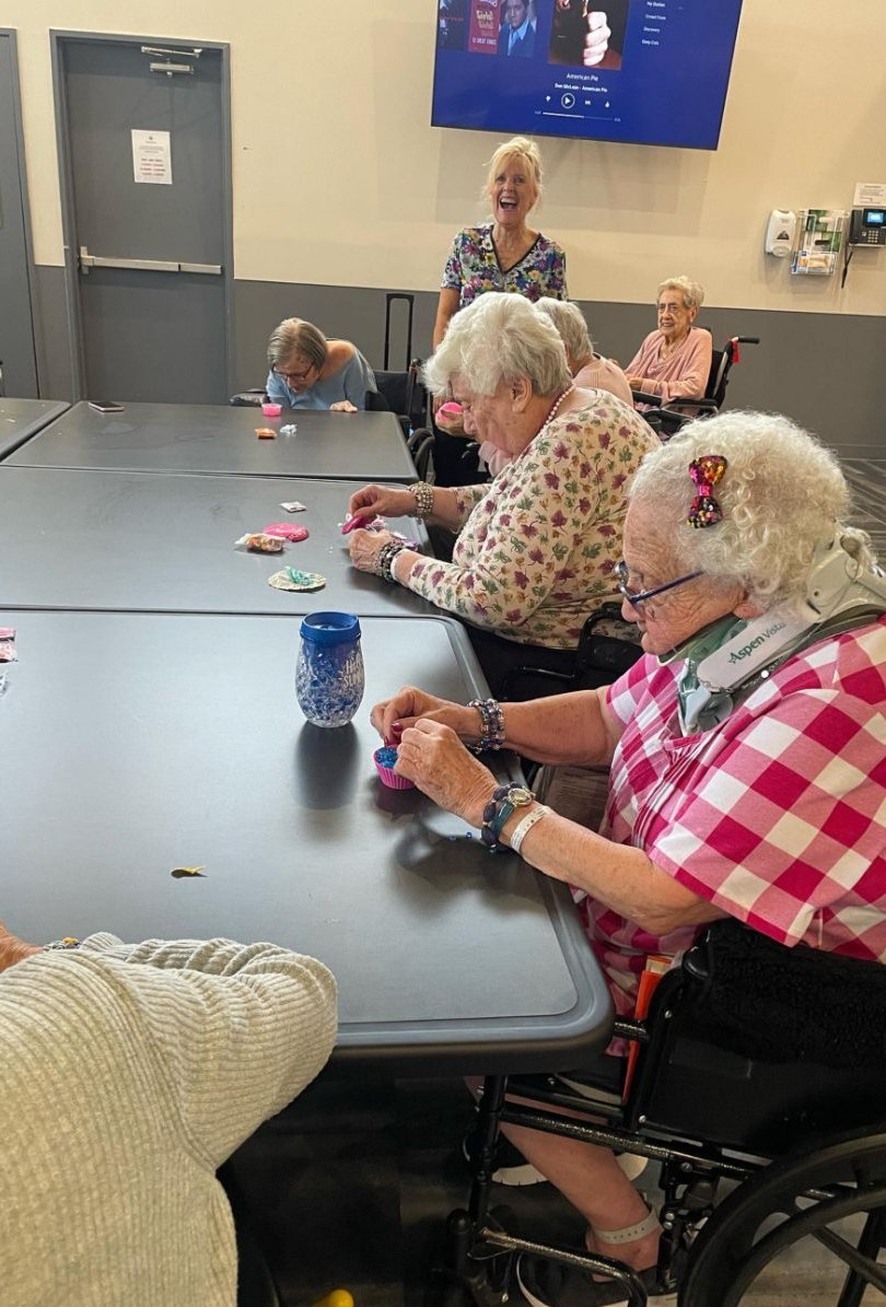 Residents at a senior community seated around tables making slime together, with a Starplay host in the background.