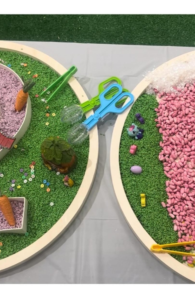Two round sensory trays filled with dyed rice, scoops and tongs, set up as a miniature garden scene.